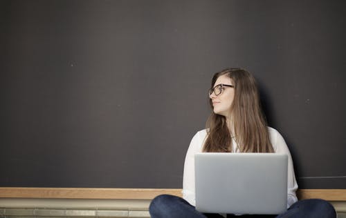 白色长袖衬衫和蓝色牛仔牛仔裤，同时使用笔记本电脑的女人 · 免费素材图片