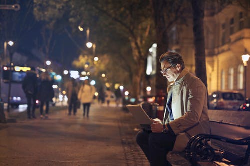 坐在长凳上，使用macbook的棕色外套的男人 · 免费素材图片