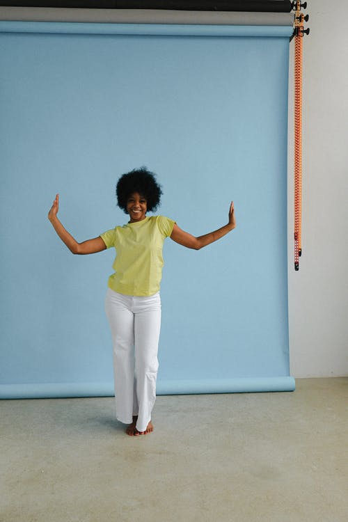 绿色的衬衫和白色的裤子，站在蓝色的墙壁旁边的女人 · 免费素材图片