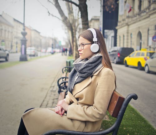女人坐在黑色和棕色的长椅上，听听音乐 · 免费素材图片