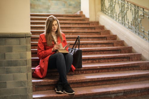 红色外套坐在棕色楼梯上的女人 · 免费素材图片