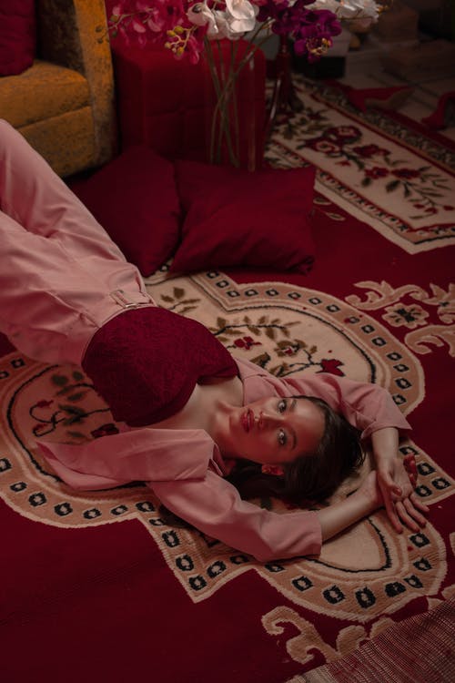 女人穿着粉红色的西装外套和粉红色的裤子躺在红色和白色的花地毯 · 免费素材图片