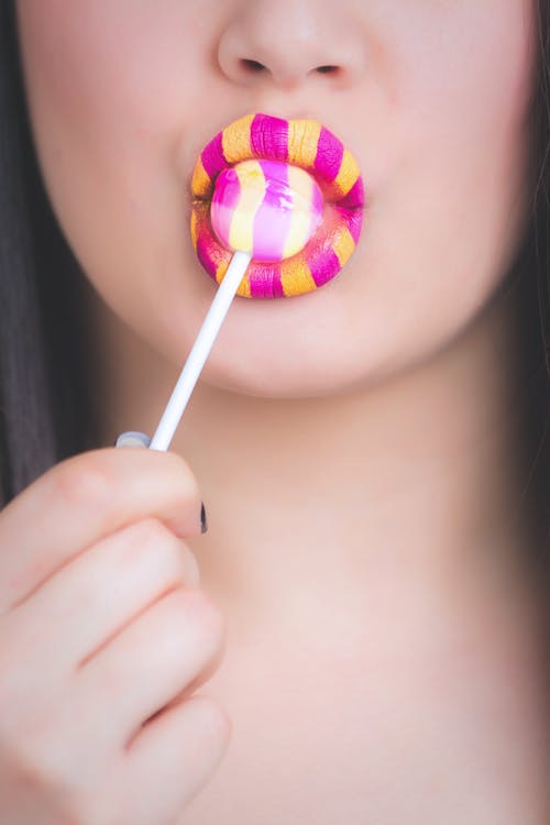 黄色和粉红色的唇膏吃棒棒糖的女人 · 免费素材图片