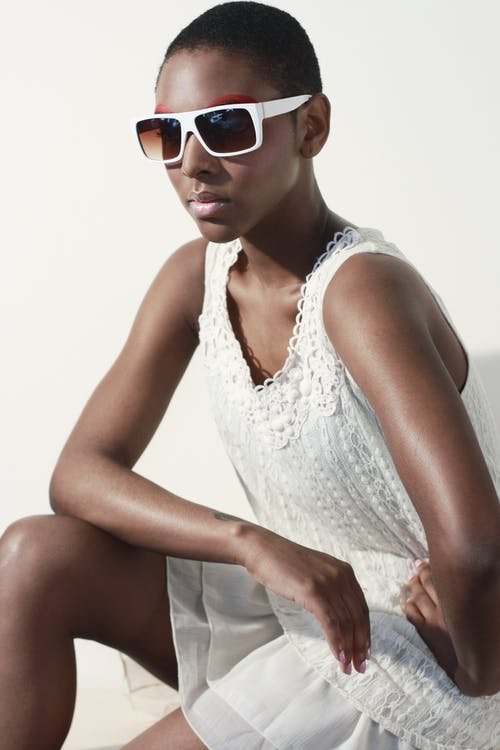 女人穿着白色背心和白色镜框太阳镜坐着摆姿势 · 免费素材图片