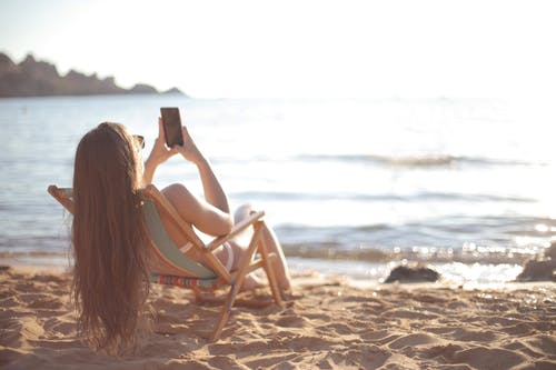 白色背心的女人坐在海滩上的白色木椅上 · 免费素材图片