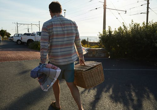 白色和棕色条纹长袖衬衫的男人携带棕色编织的篮子 · 免费素材图片
