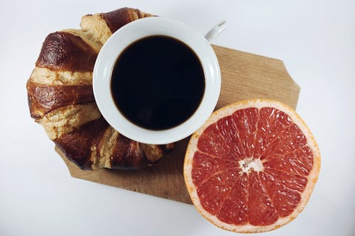 葡萄柚和羊角面包在棕色木板之间的黑咖啡 · 免费素材图片