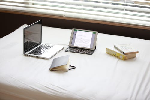 Macbook Pro在白色ipad旁边的白色织物表上 · 免费素材图片
