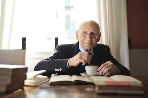 老人在明亮的房间里在桌上读书时喝热饮料 · 免费素材图片
