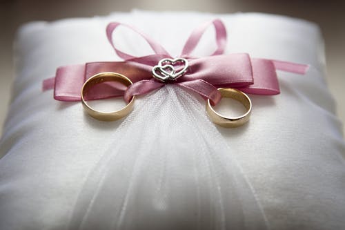 银质订婚戒指套装（带粉红色蝴蝶结装饰）在枕头上的选择性聚焦摄影 · 免费素材图片