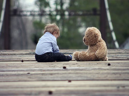 男孩与棕熊毛绒玩具坐在选择性焦点照片上 · 免费素材图片