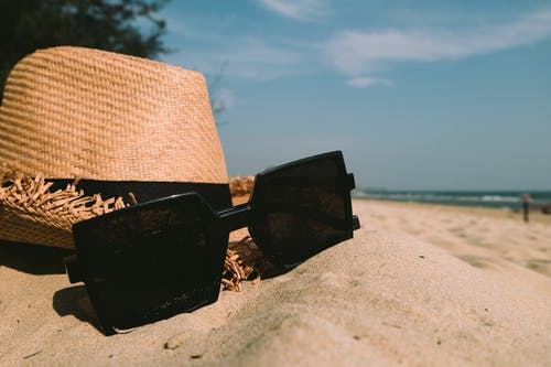 在沙滩上的太阳帽旁边的太阳镜 · 免费素材图片