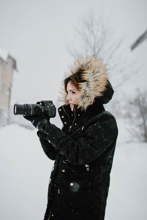 拿着黑色的单反相机的黑色和棕色皮大衣夹克的女人 · 免费素材图片