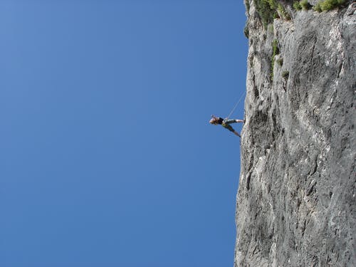 男子站在岩石上对湛蓝的天空 · 免费素材图片
