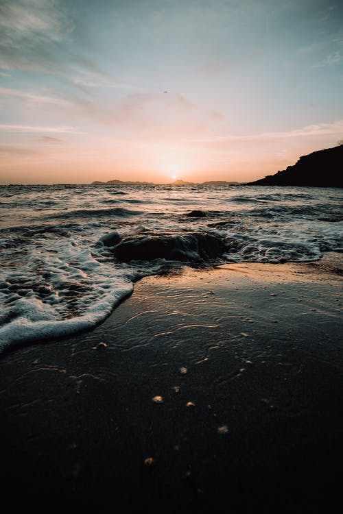 海浪在日落期间在海岸上崩溃 · 免费素材图片