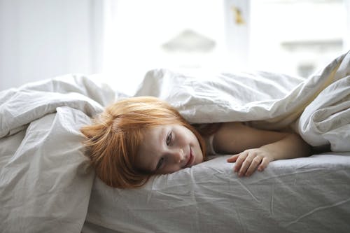 孩子躺在床上覆盖她的身体在毯子上 · 免费素材图片