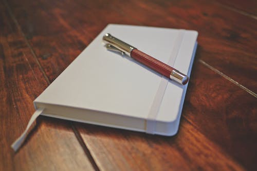 白色笔记本上的棕色笔 · 免费素材图片