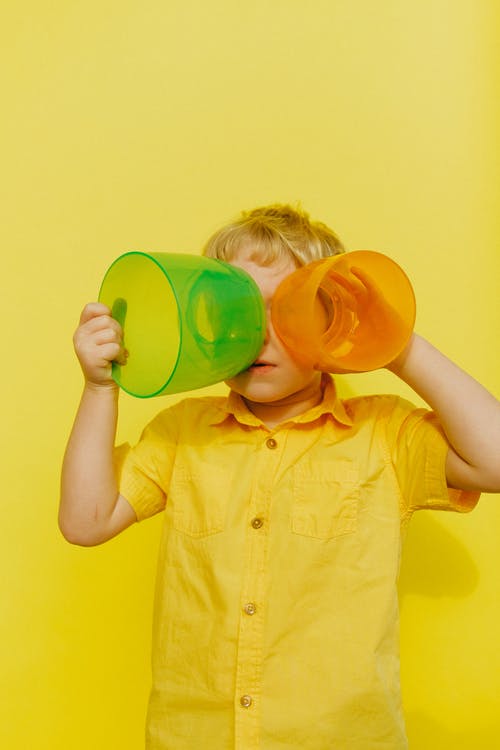 黄色按钮的衬衫的男孩拿着黄色和绿色的塑料容器 · 免费素材图片