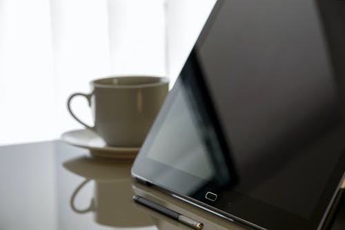 黑色平板电脑旁边茶杯与桌上的茶碟 · 免费素材图片
