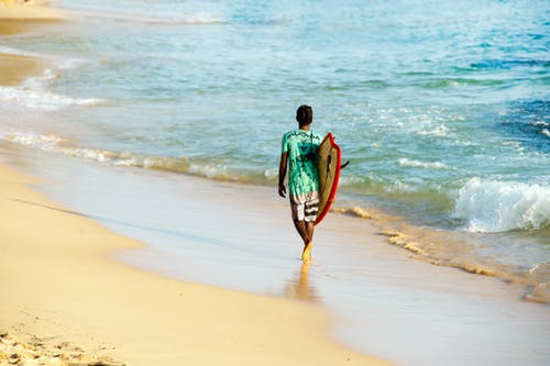按住冲浪板在岸上行走的人 · 免费素材图片