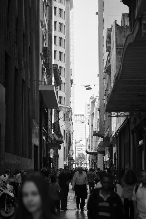 在建筑物之间的街道上行走的人的灰度照片 · 免费素材图片