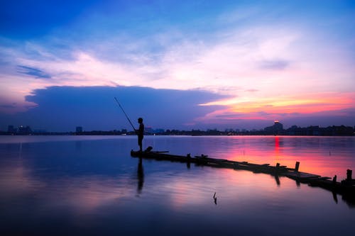 男子手持钓鱼竿在水体上的剪影 · 免费素材图片