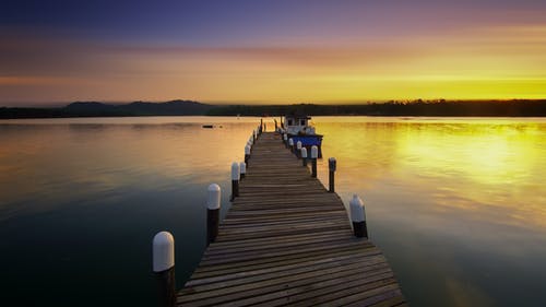 在日落期间在水面上的棕色木码头旁边的白色游艇 · 免费素材图片
