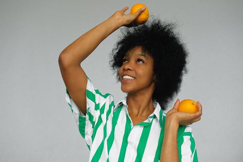 拿着橙色水果的绿色和白色条纹polo衫的女人 · 免费素材图片