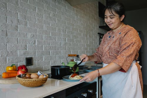 烹调开胃意粉用站立在桌上的调味汁的美满的高级种族妇女用新鲜蔬菜和鸡蛋在厨房里 · 免费素材图片