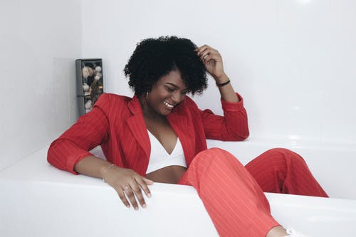 坐在浴缸里的红色细条纹西装笑女人的照片 · 免费素材图片
