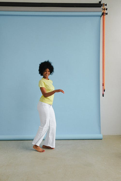绿色的衬衫和白色的裤子，站在蓝色的墙壁旁边的女人 · 免费素材图片