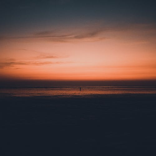 一个人在日落时分在海边散步的剪影照片 · 免费素材图片