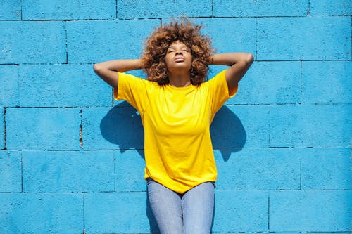 穿着黄色衬衫，倚着蓝色砖墙的一位女士 · 免费素材图片