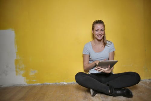 女人坐在木地板上使用平板电脑 · 免费素材图片