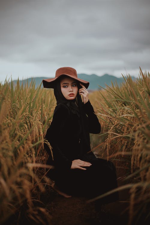 黑色长袖衬衫和棕色的帽子，坐在棕色草地上的女人 · 免费素材图片