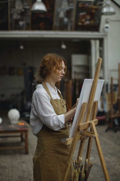 白色长袖衬衫和棕色围裙站立时绘图的女人 · 免费素材图片