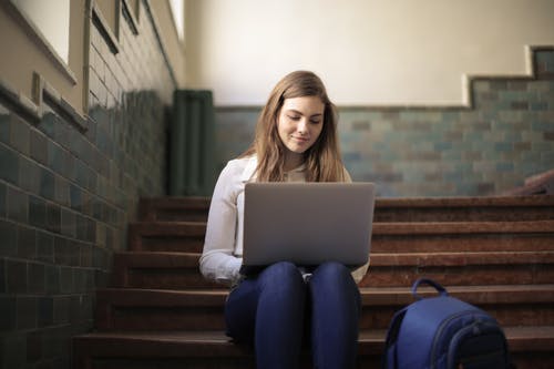 女人坐在楼梯上时使用一台笔记本电脑 · 免费素材图片