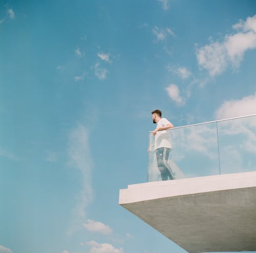 白色长袖衬衫和慢跑站在阳台上的男人 · 免费素材图片