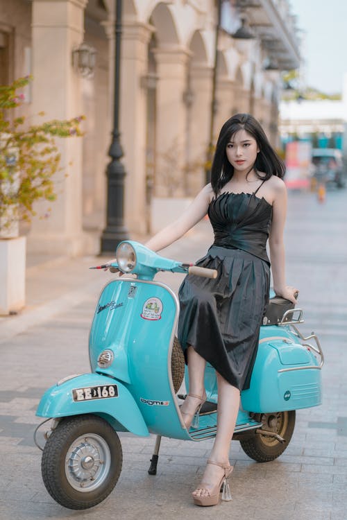 黑色无袖连衣裙骑蓝色摩托车的女人 · 免费素材图片
