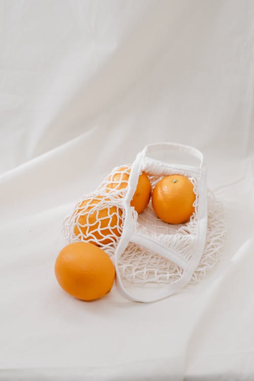 白色网格袋上的四个橙色水果 · 免费素材图片