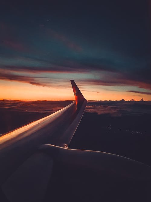 日落期间飞机机翼越过云层 · 免费素材图片