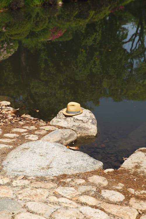 草帽位于湖堤上的石头上 · 免费素材图片