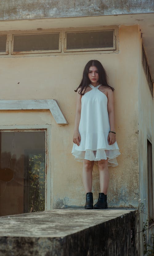 站在混凝土墙上的白色连衣裙的女人 · 免费素材图片
