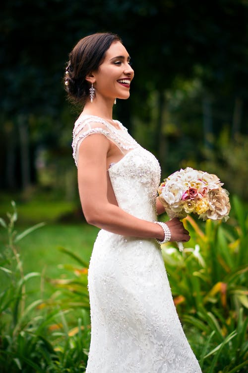 拿着花束花束微笑的白色花卉婚礼礼服的妇女 · 免费素材图片
