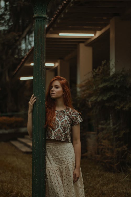 女人穿着花衬衫站在绿色的岗位附近 · 免费素材图片