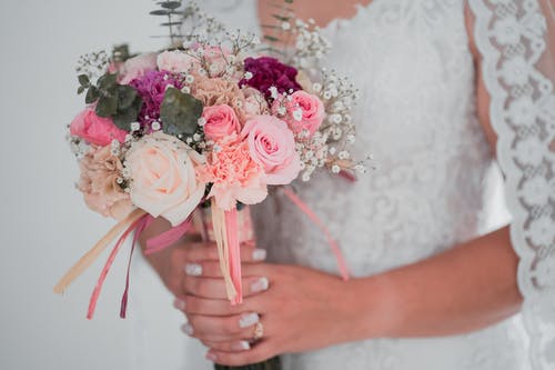 拿着桃红色和白色玫瑰花束的白色婚礼礼服的妇女 · 免费素材图片