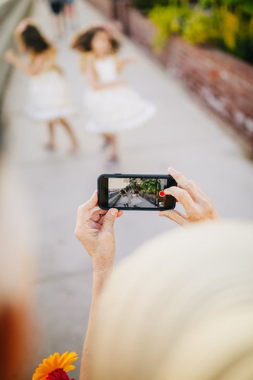 拿着黑智能手机的人拍在街道上跳舞的孩子的照片 · 免费素材图片
