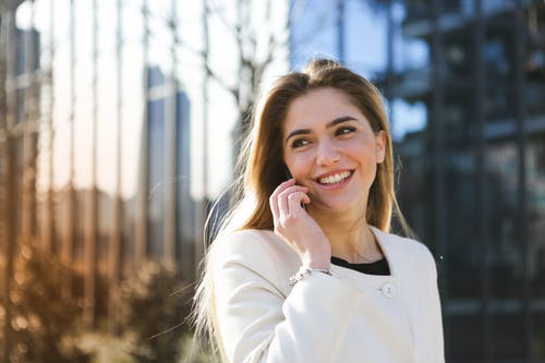 女人穿着白色长袖外套在电话上交谈时微笑的选择性焦点照片 · 免费素材图片
