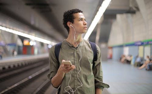 耳塞的年轻的族裔人在当代地铁站等待运输时听音乐 · 免费素材图片