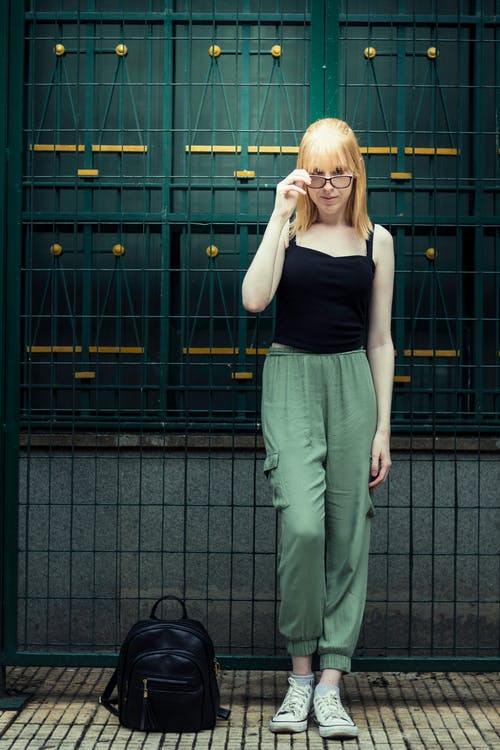 黑色背心和绿色的裤子，站在绿门旁边的女人 · 免费素材图片